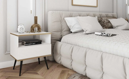 Szafka nocna z szufladą Luxury biała elegancki design korpus zwieńczony złotą listwą szafka z ryflowanym frontem czarne wysokie nogi